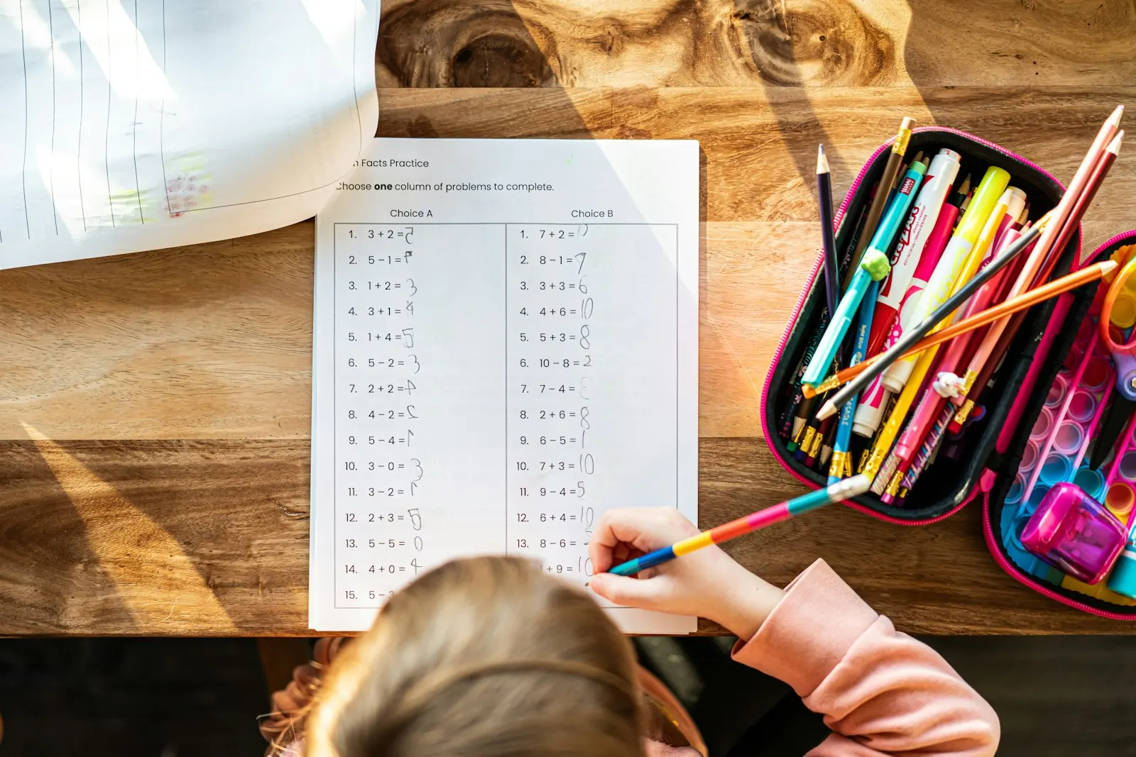 A child's math worksheet on a wooden table with a pencil case